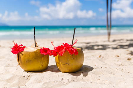 Two coconut cocktails on white sand beach next to clean sea blue water. Vacation and travel conceptの写真素材