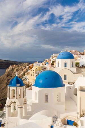 Famous three blue domes in Santorini. Oia village. White church, blue dome. Cloudy sky.の写真素材