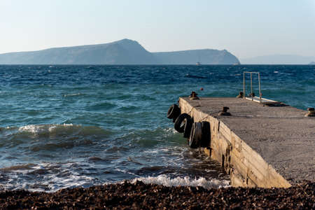 A pier in the sea, black car tires, island in the backgroundの写真素材