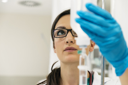 Young woman doctor anesthesiologist dressed in green gown, puts the dropper in hospital roomの写真素材