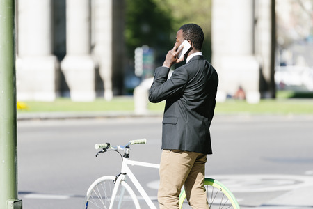Handsome african man with mobile phone and fixed gear bicycle in the street.の写真素材