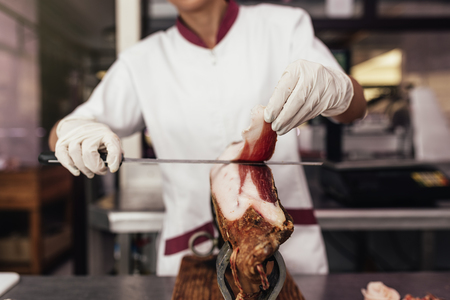 Pretty butchery woman cutting ham with knife.の写真素材