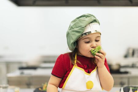 Happy girl eating broccoli in a kitchen.の写真素材