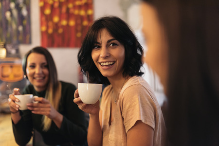 Three beautiful women drinking coffee and chatting in cafeの写真素材