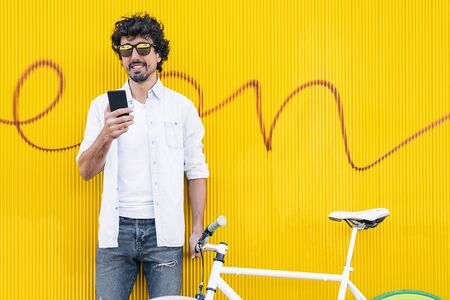 Outdoor portrait of handsome young man with mobile phone and fixed gear bicycle in the street.の写真素材