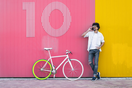 Outdoor portrait of handsome young man with mobile phone and fixed gear bicycle in the street.の写真素材