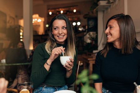 Two beautiful women drinking coffee and chatting in cafe