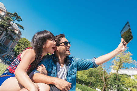 Young happy couple using tablet sitting in the park