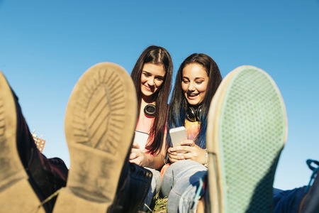Two Beautiful Teenage Girls Using Mobile In Parkの写真素材
