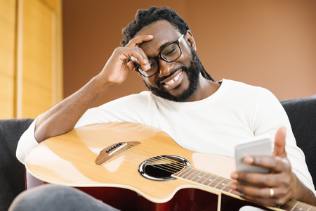 Guitarist with guitar using mobile in his home.の写真素材