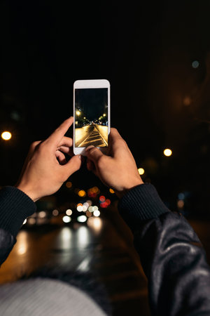Boy takes a photograph of a street at night.