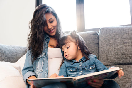 Mother reading a book to her daughter at home.の写真素材