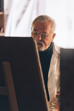 Old man artist painting oils in his studio. Artist Concept.の写真素材