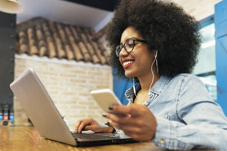 Beautiful afro american woman using mobile and laptop in the coffee shop. Communication concept.の写真素材