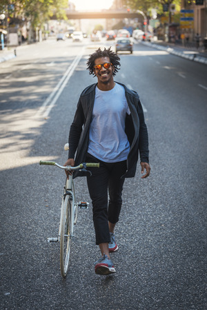 Handsome afro man walking with his bike in the street.の写真素材