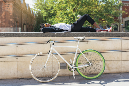 Handsome afro man relaxing near his bike in the street.の写真素材