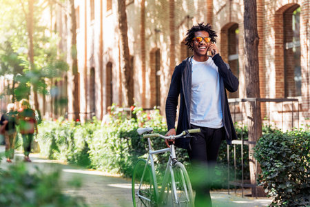 Afro young man using mobile phone and fixed gear bicycle in the street.