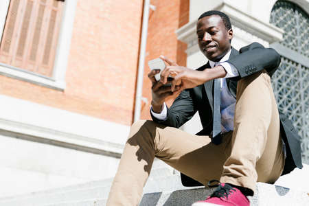 Portrait of Handsome african man smiling when he is using his mobile in the street.の写真素材