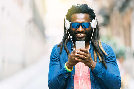 Outdoor Portrait Of Handsome African Young Man Writing Message And Listening Music.の写真素材