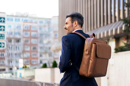 Businessman with backpack walking in cityの写真素材