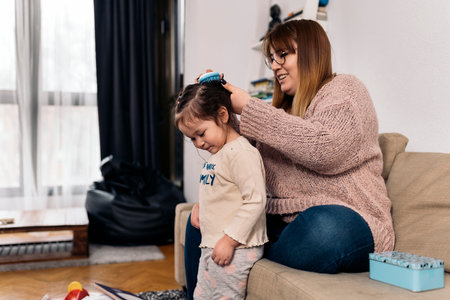 Stock photo of happy woman combing her daughter's hair in the living room.