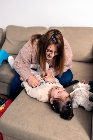 Stock photo of smiley woman playing with her cute daughter on the sofa.