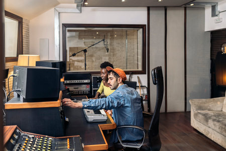 Stock photo of black woman working with male producer in music studio.