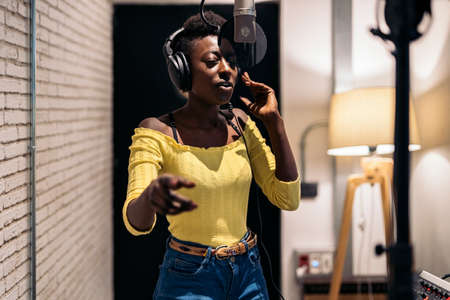 Stock photo of beautiful black woman singing and using microphone in music studio.の写真素材