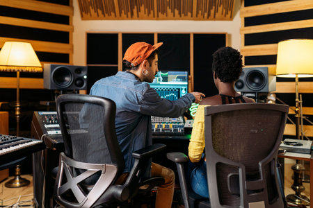 Stock photo of male music producer working with black singer in professional music studio.