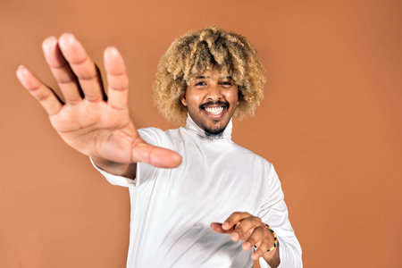 Stock photo of cool afro man smiling and looking at camera in studio shot against brown background.