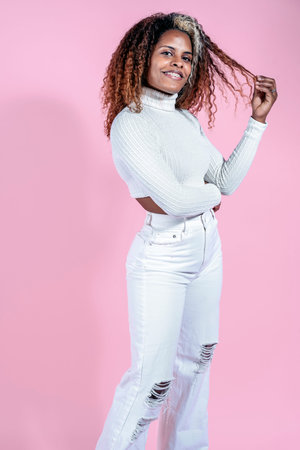 Happy black woman with curly hair smiling in studio shot against pink background.