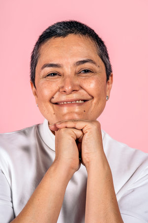Stock photo of smiley woman with short gray hair having fun in studio shot against pink background.