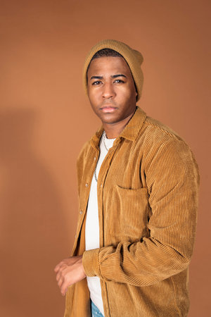 Young man wearing hat posing in studio shot against brown background.