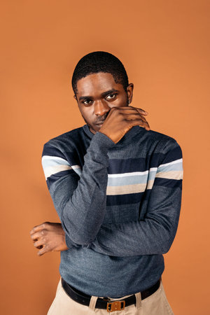 Stock photo of young black man wearing elegant clothes posing in studio shot against brown background.の写真素材