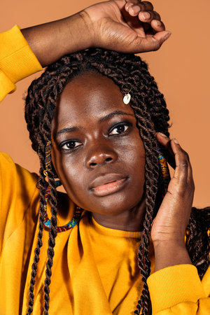 Stock photo of confident black woman with braids posing in studio shot against brown background.