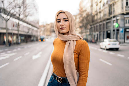Pretty young muslim woman wearing pink head scarf smiling and looking at camera in the street.の写真素材