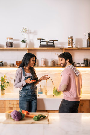 Beautiful black woman using her phone in the kitchen while her boyfriend cooks.
