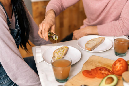Unrecognized man sitting in the kitchen next to her girlfriend preparing delicious breakfast.の写真素材