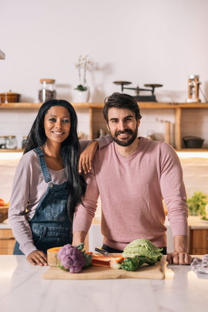 Cute couple looking at camera and preparing lunch together in the kitchen at home.
