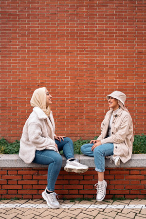 Cheerful young women wearing hijab talking and sitting in a bench.の写真素材