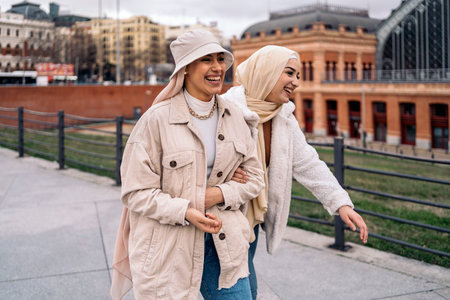 Cheerful young women wearing hijab laughing and walking in the street.の写真素材