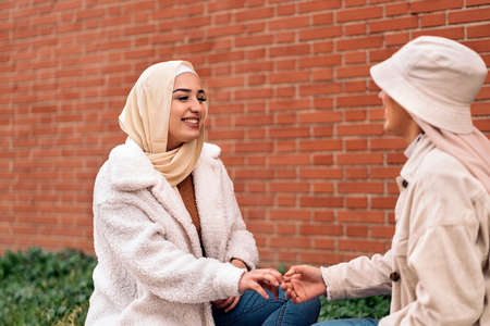 Cheerful young women wearing hijab talking and sitting in a bench.の写真素材