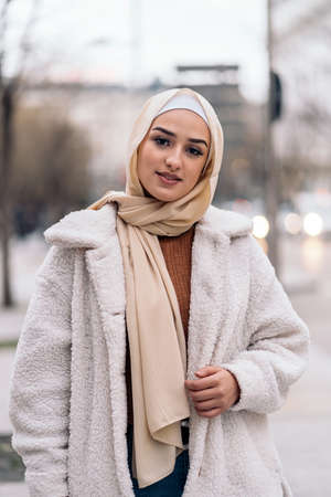 Smiley muslim woman wearing head scarf posing and looking at camera in the street.の写真素材