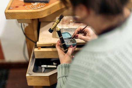 Concentrated craftswoman using blowtorch in jewelry workshop.