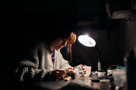 Stock photo of concentrated woman using paint in jewelry workshop.の写真素材