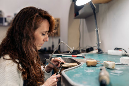 Stock photo of focused woman working in jewelry workshop.