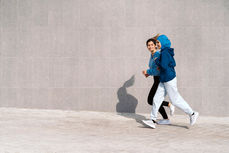 Active young female friends running in the street and smiling. One of them is wearing a hijab.の写真素材