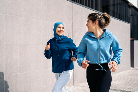 Cheerful muslim woman wearing hijab running in the street with her friend and having fun.の写真素材