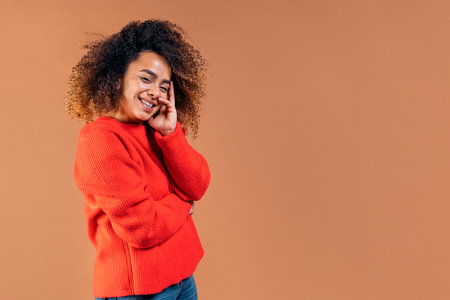 Beautiful black woman with curly hair smiling and looking at camera in studio shot against brown background.の写真素材