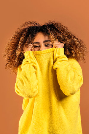 Cheerful young black woman smiling and looking at camera in studio shot against brown background.の写真素材